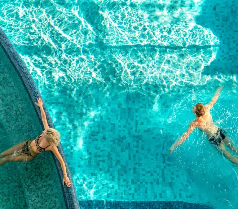 A couple relaxes in a bright swimming pool with clear water and light reflections.